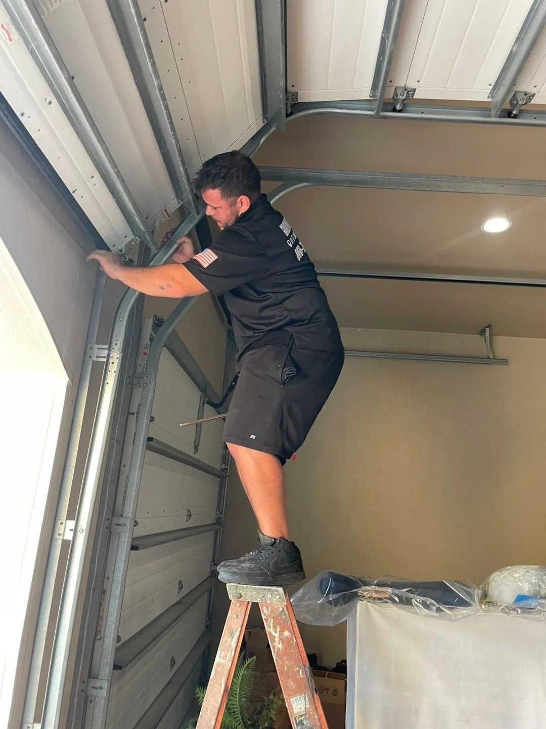 Technician on a stepladder reaching the top of a garage door track