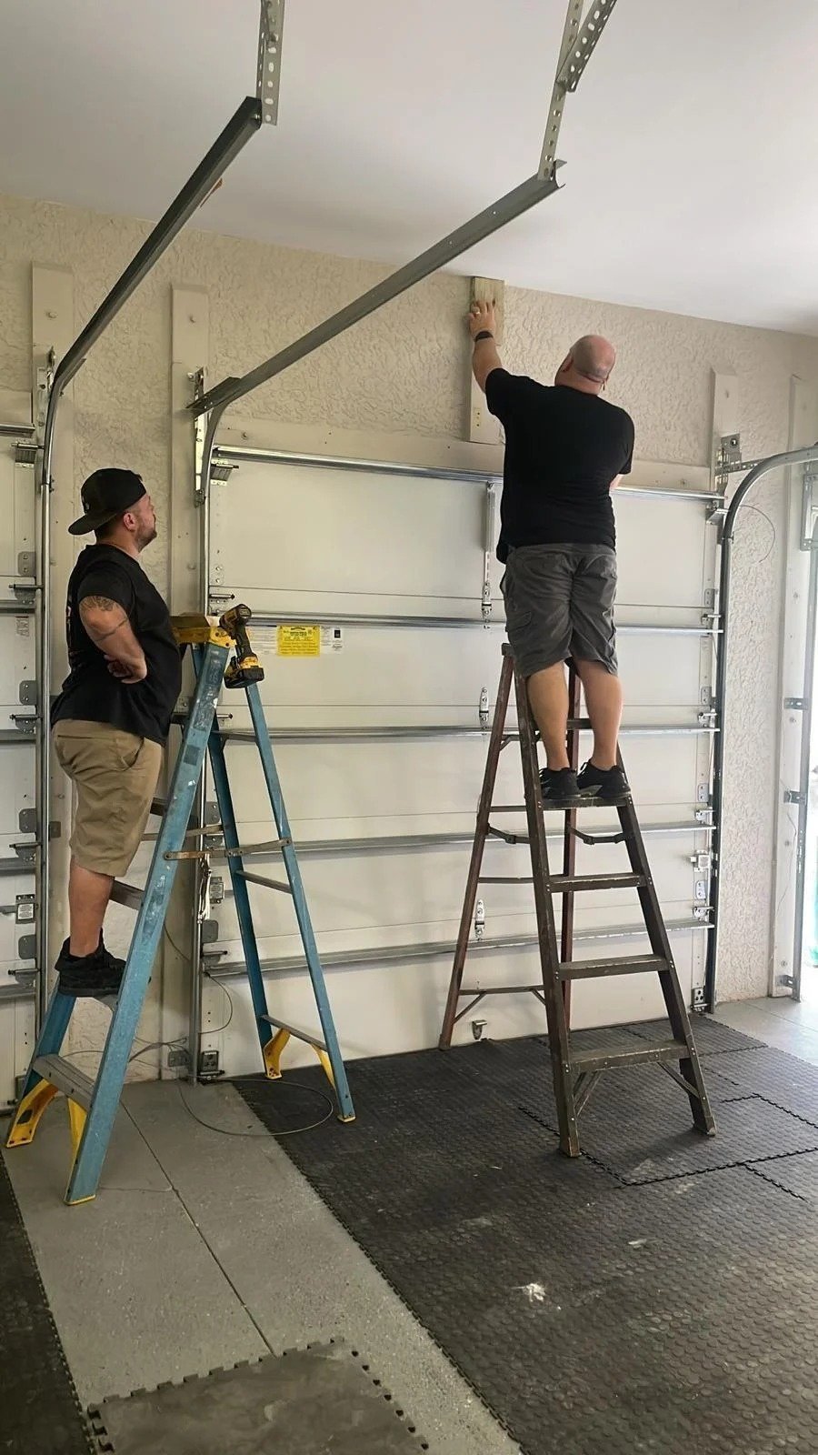 Two technicians on ladders adjusting the top section of a sectional garage door