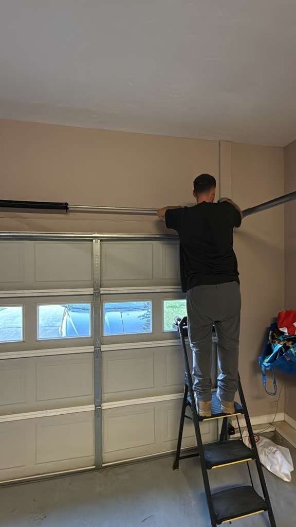Technician on a stepladder at the top of a paneled garage door