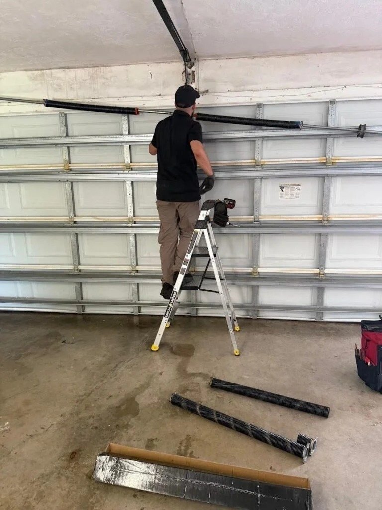 Technician on a stepladder beside a garage door with steel shafts on the floor
