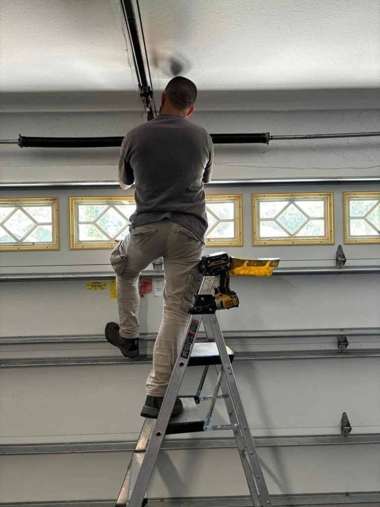 Technician on a ladder working on a garage door with diamond-pattern windows