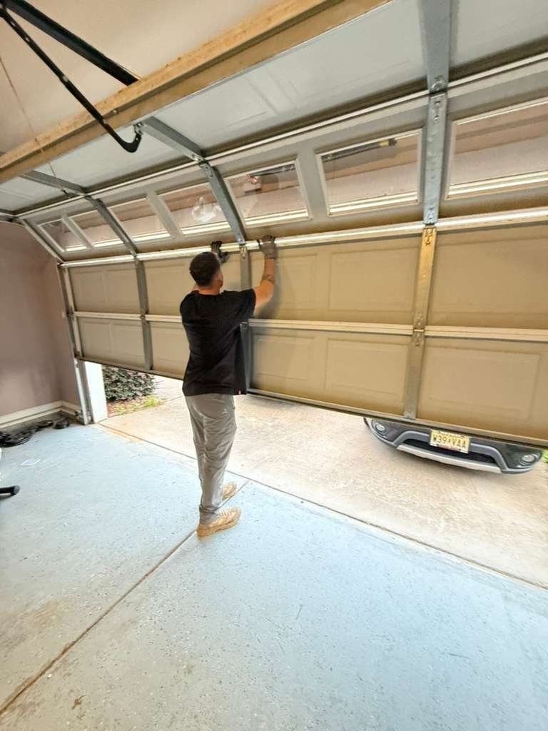 Technician reaching up to the track of a tan sectional garage door from inside the garage
