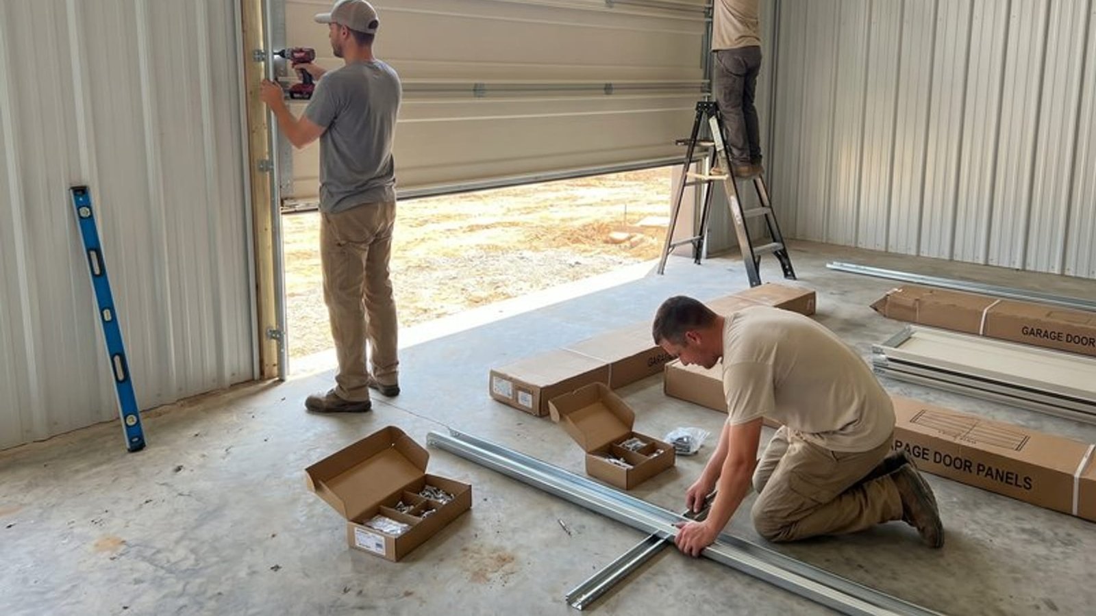 Two technicians unpacking door hardware and checking a level in an open garage
