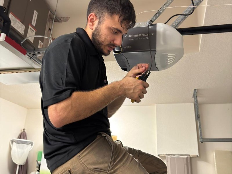 Technician in a black shirt working on a garage door opener unit with a tool