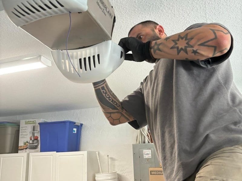 Technician with a tattooed forearm reaching up to a garage door opener head unit
